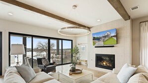 A spacious living room with a large window, a fireplace, and a mounted TV. - Waterhouse at Lake LBJ Residence II, 6 King Bedrooms|  Pool, Spa, Boat & PWC Lift, Slide  (Kingsland)