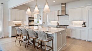 A modern kitchen with white cabinetry, a large island with bar stools, pendant lighting, and a stainless steel stove. - Waterhouse at Lake LBJ Residence II, 6 King Bedrooms|  Pool, Spa, Boat & PWC Lift, Slide  (Kingsland)