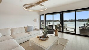 A modern living room with a large window, a sofa, a coffee table, and a view of the water. - Waterhouse at Lake LBJ Residence II, 6 King Bedrooms|  Pool, Spa, Boat & PWC Lift, Slide  (Kingsland)