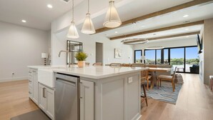 A spacious kitchen with a large island, modern pendant lighting, and a view to the outdoors. - Waterhouse at Lake LBJ Residence II, 6 King Bedrooms|  Pool, Spa, Boat & PWC Lift, Slide  (Kingsland)
