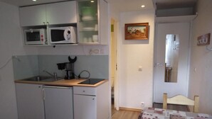 A compact kitchen with a microwave, coffee maker, and a small sink. There is a bed with a patterned bedspread and a chair. - 100m from ski lifts, 7th floor, balcony, tv, ski locker, 15m², La Plagne (La Plagne)