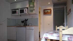 A compact kitchen with white appliances, a wooden table with a heart-patterned tablecloth, and a door leading to another room. - 100m from ski lifts, 7th floor, balcony, tv, ski locker, 15m², La Plagne (La Plagne)