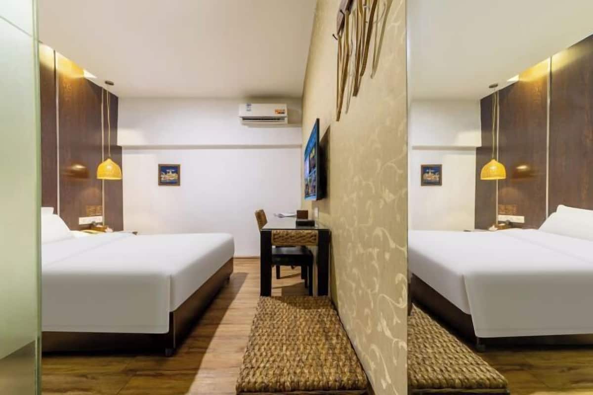 A hotel room with two beds, a small table, a chair, and a TV on the wall.