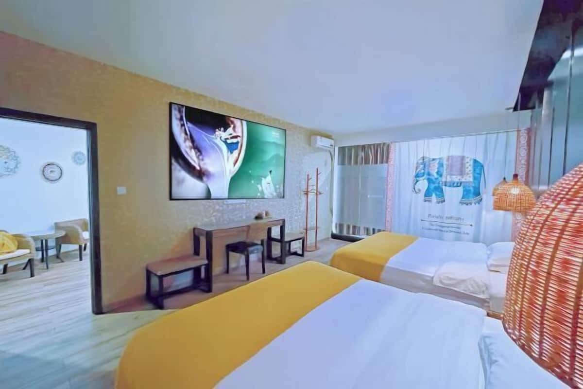 A hotel room with two beds, a desk, a chair, a TV, and a window with curtains.