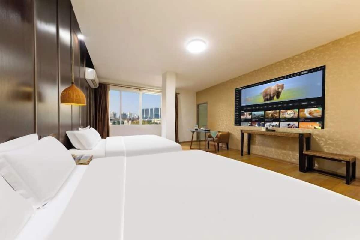 A hotel room with a large bed, a desk with a computer, and a wall-mounted TV displaying a bear.