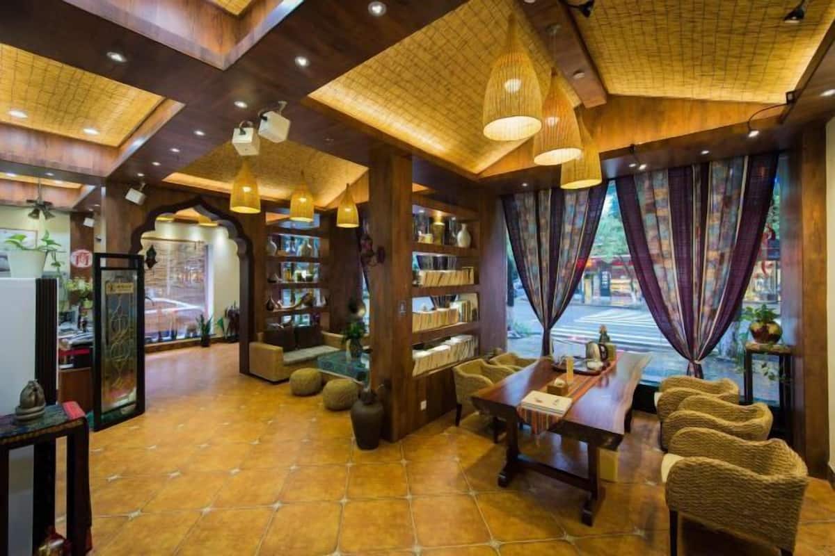 A cozy interior with a wooden ceiling, shelves with books, a dining area, and a view through large windows.