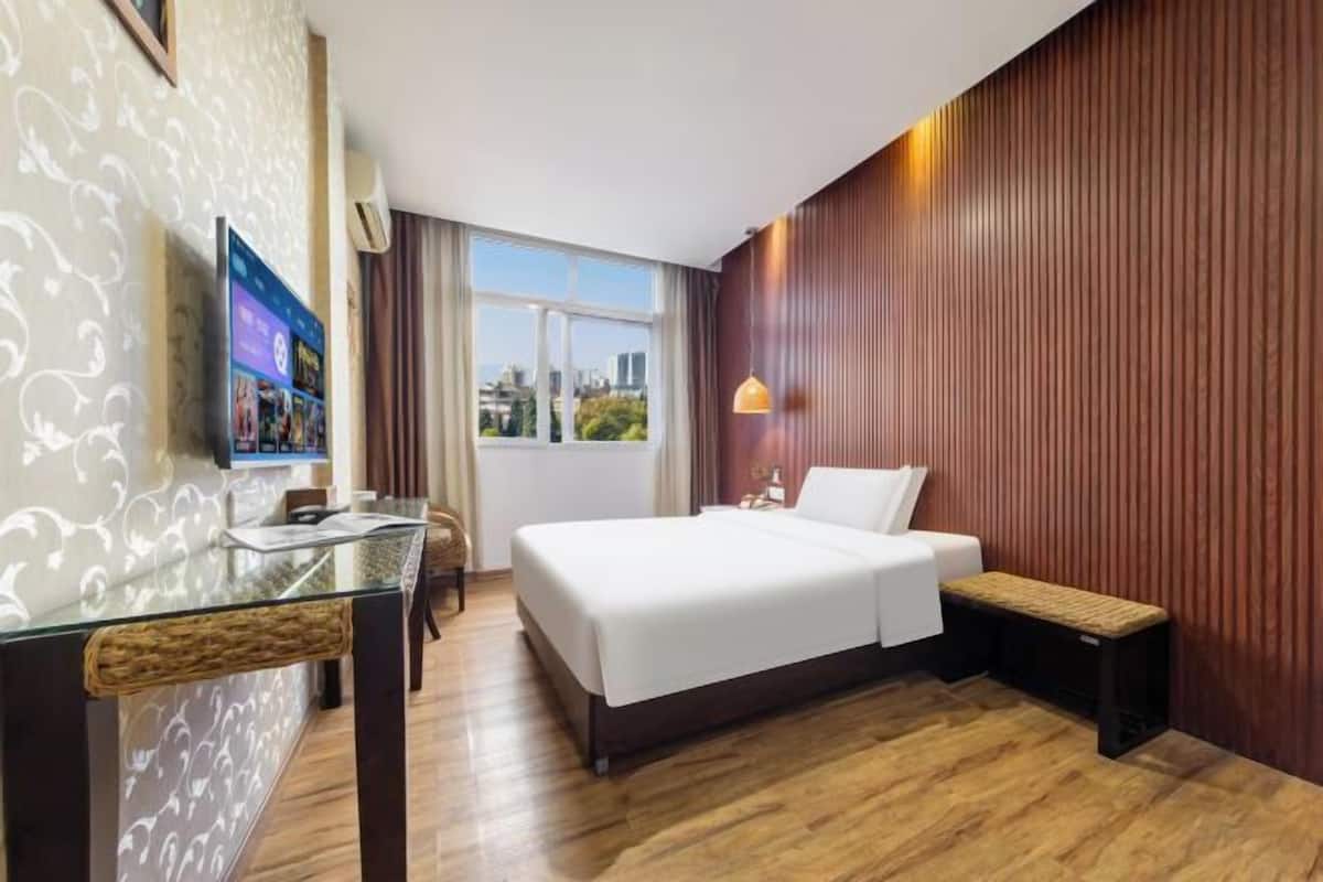 A hotel room with a bed, a TV, a desk, and a window with a city view.