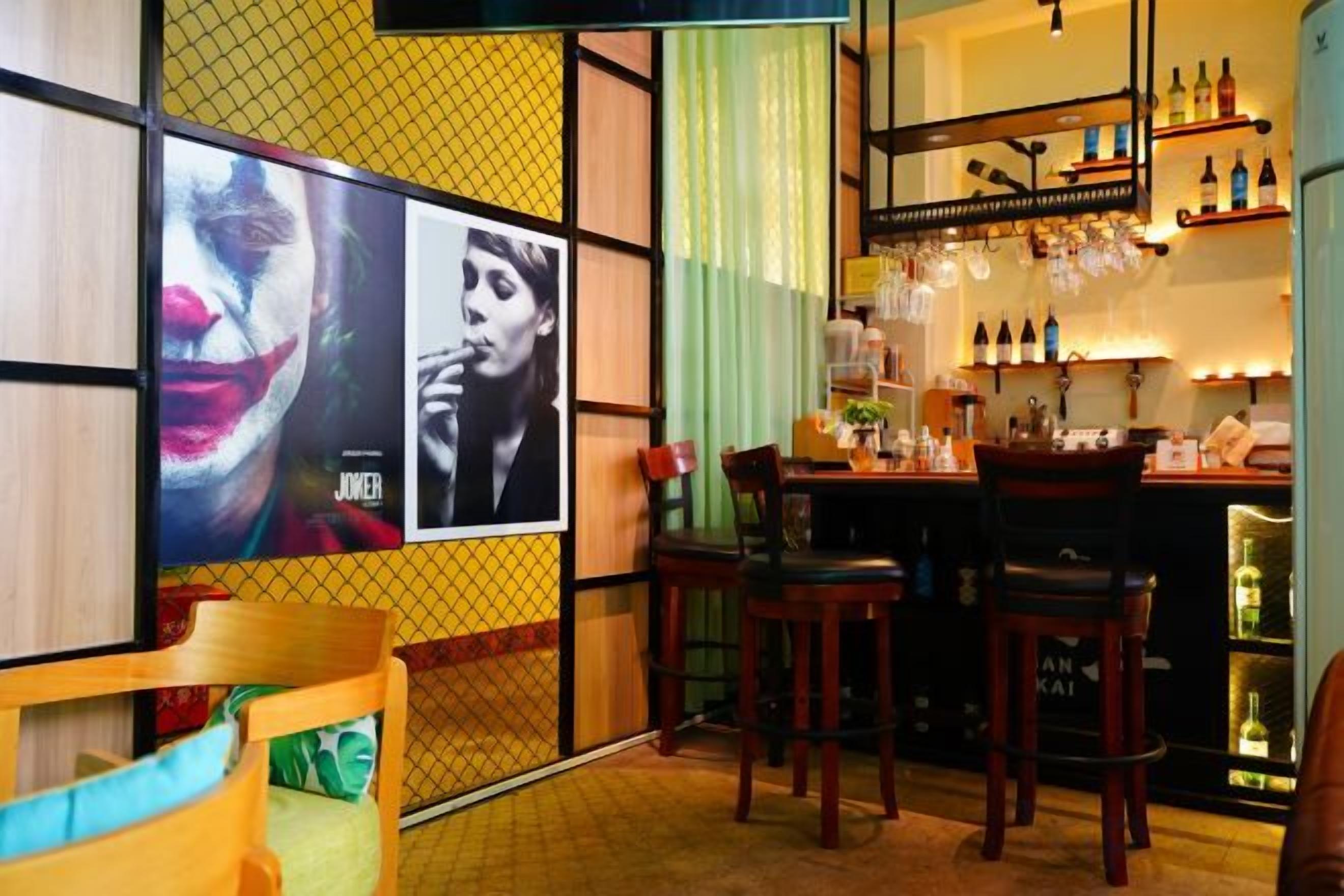 A bar area with stools, a bar counter, and a shelf with bottles.