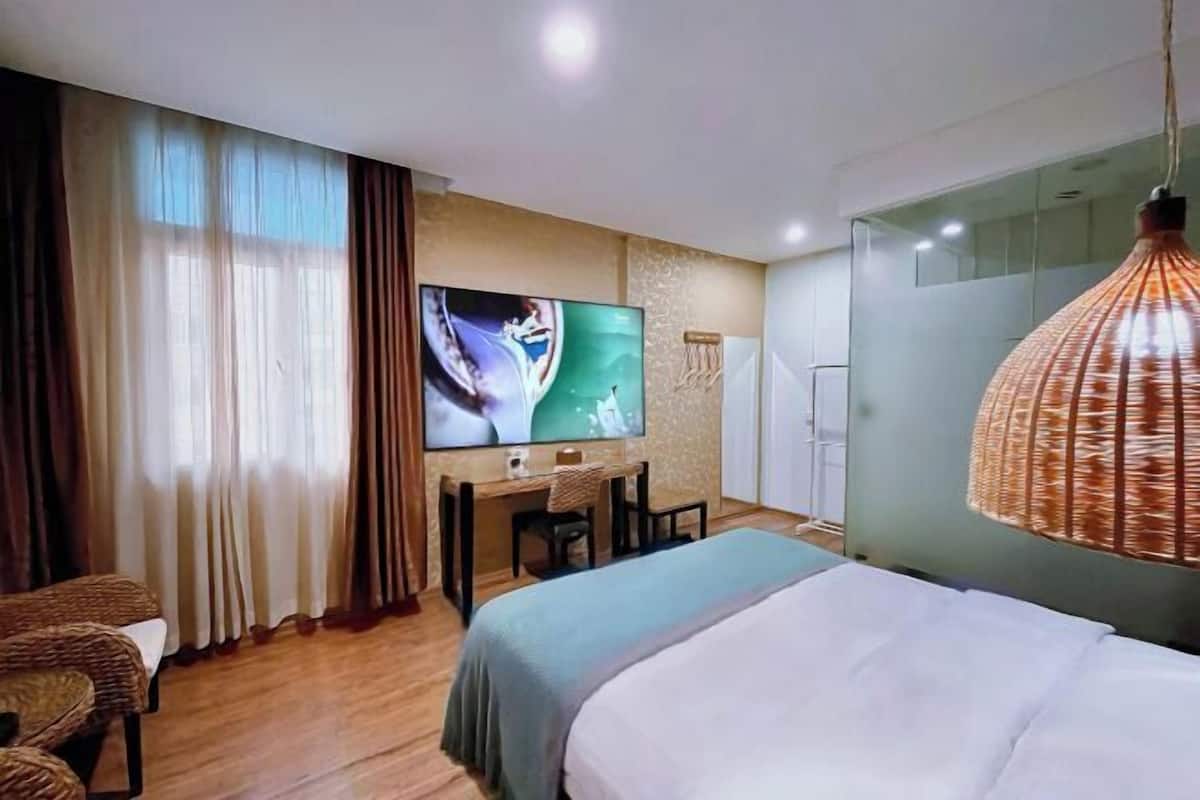 A hotel room with a bed, a desk with a chair, a television, and a large window with curtains.