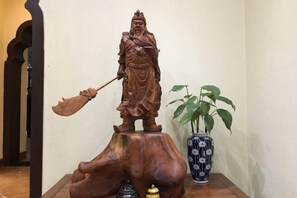 A wooden statue of a figure holding a staff, placed on a wooden base.