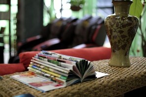 A woven table with a stack of magazines and a vase.