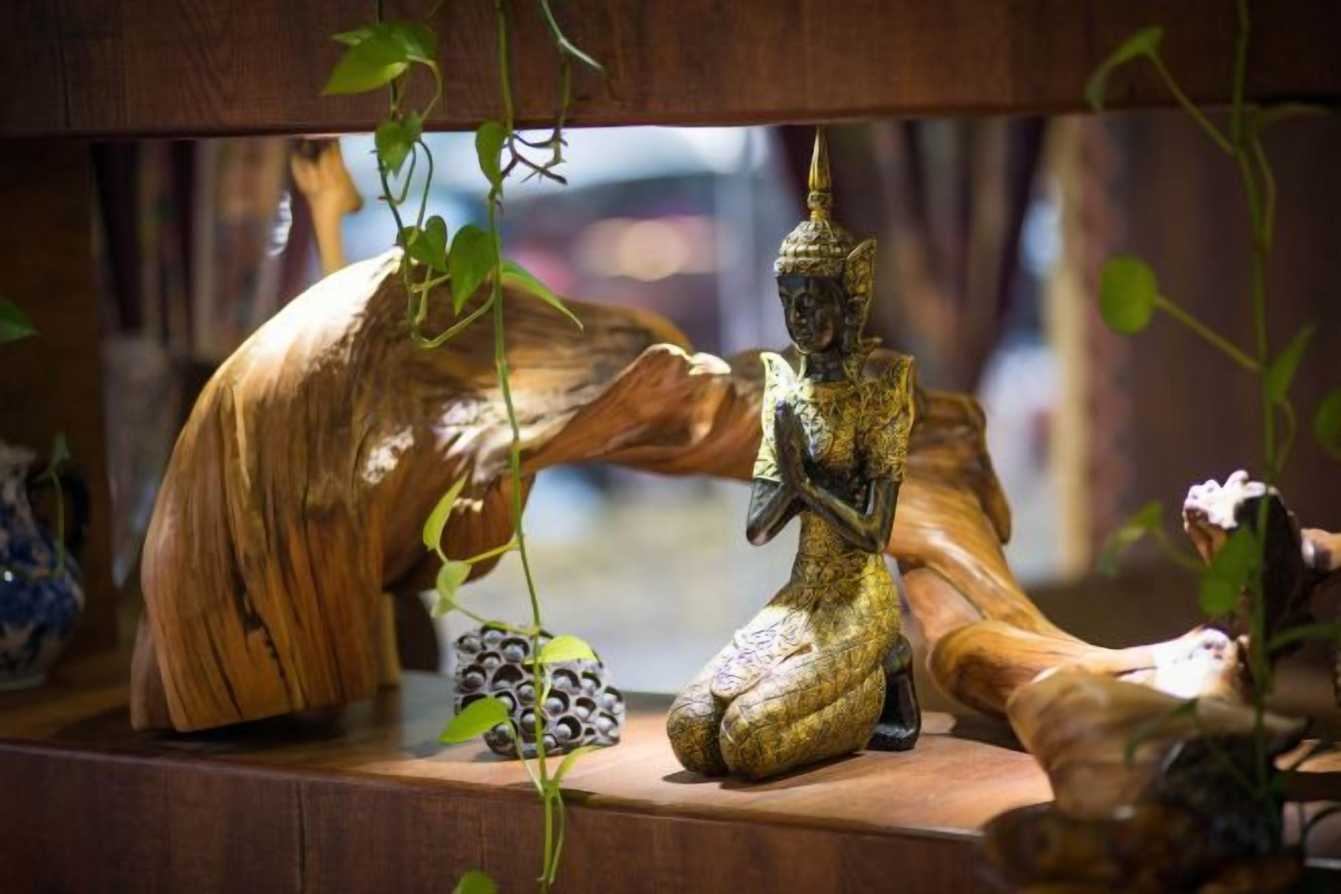 Una repisa de madera con una estatua, un tronco de madera tallado y un pequeño objeto decorativo.
