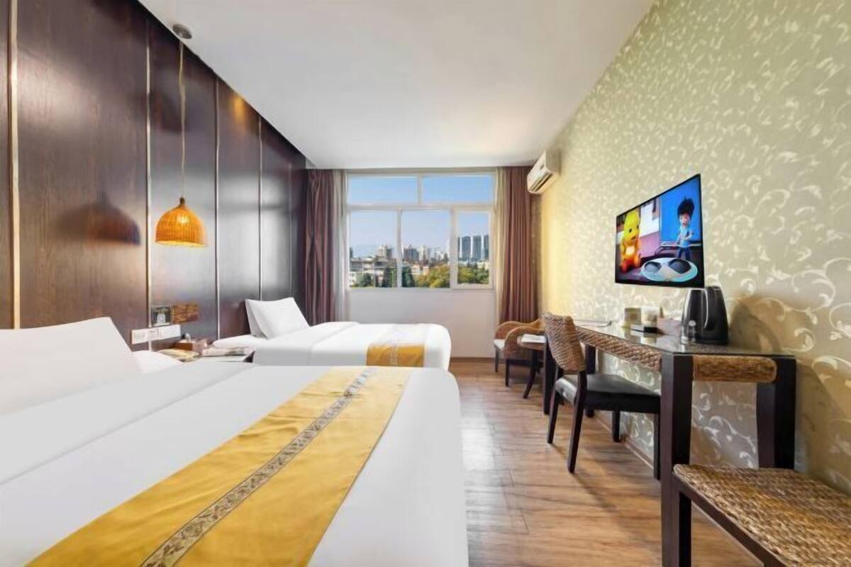 A hotel room with two beds, a TV, a desk, and a view of the city.