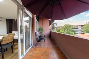 A balcony with a dining area, a large umbrella, and a view of surrounding buildings. - Bati Yangguang Chain Hotel Meizhou Meilong (Meizhou)
