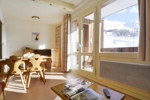 Een kamer met een houten eettafel en stoelen, een bank en een groot raam met uitzicht op een besneeerd landschap.