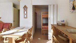 A room with a wooden table and chairs, a bunk bed, and a small desk with a basket.