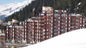 A multi-story hotel with a modern architectural design, located in a mountainous area with snow-covered peaks in the background.