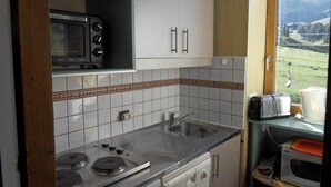 A compact kitchen with a microwave, stove, and sink. It features a tiled backsplash and a view of a mountainous landscape through a window.