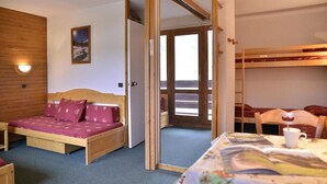 A room with a wooden bed, a small sofa, a table with a book, and a door leading to a balcony.