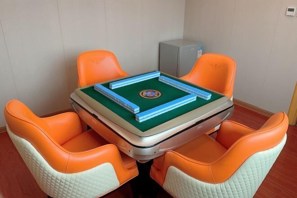 A small room with a table set for two, featuring a green felt table and two orange chairs with white cushions.