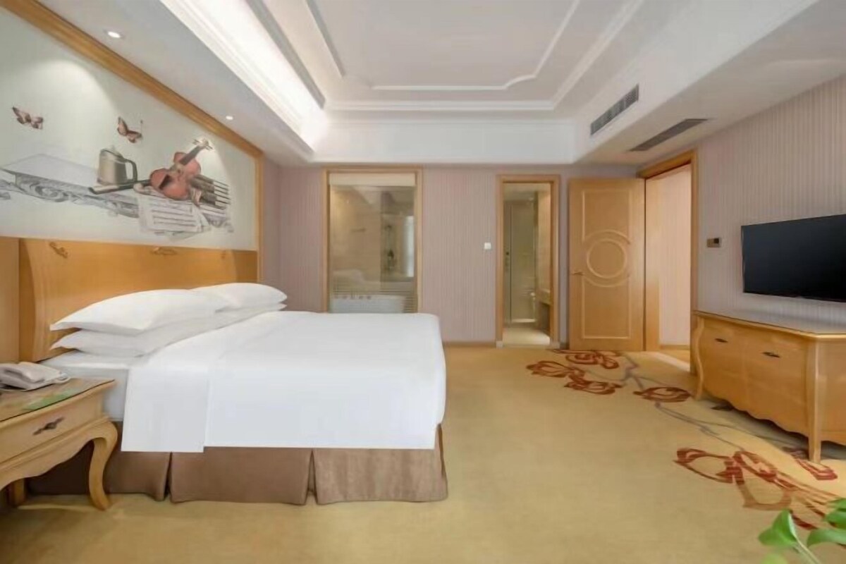 A hotel room with a bed, a TV, a desk, and a door leading to a bathroom.