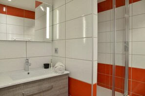 Ein modernes Badezimmer mit einem weißen Waschbecken, einem Spiegel und einer Duschkabine aus Glas.