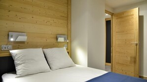 Ein Schlafzimmer mit einem hölzernen Kopfende, einem Bett mit weißer Bettwäsche, zwei Nachttischlampen und einer Holztür.