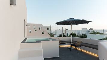 Una terraza en la azotea con un jacuzzi cubierto de vidrio, mobiliario exterior y vistas a la ciudad.