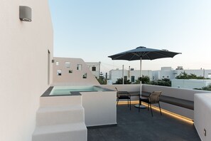 A rooftop terrace with a glass-enclosed hot tub, outdoor seating, and a view of the cityscape. - Elements Cozy Suites (Santorini)