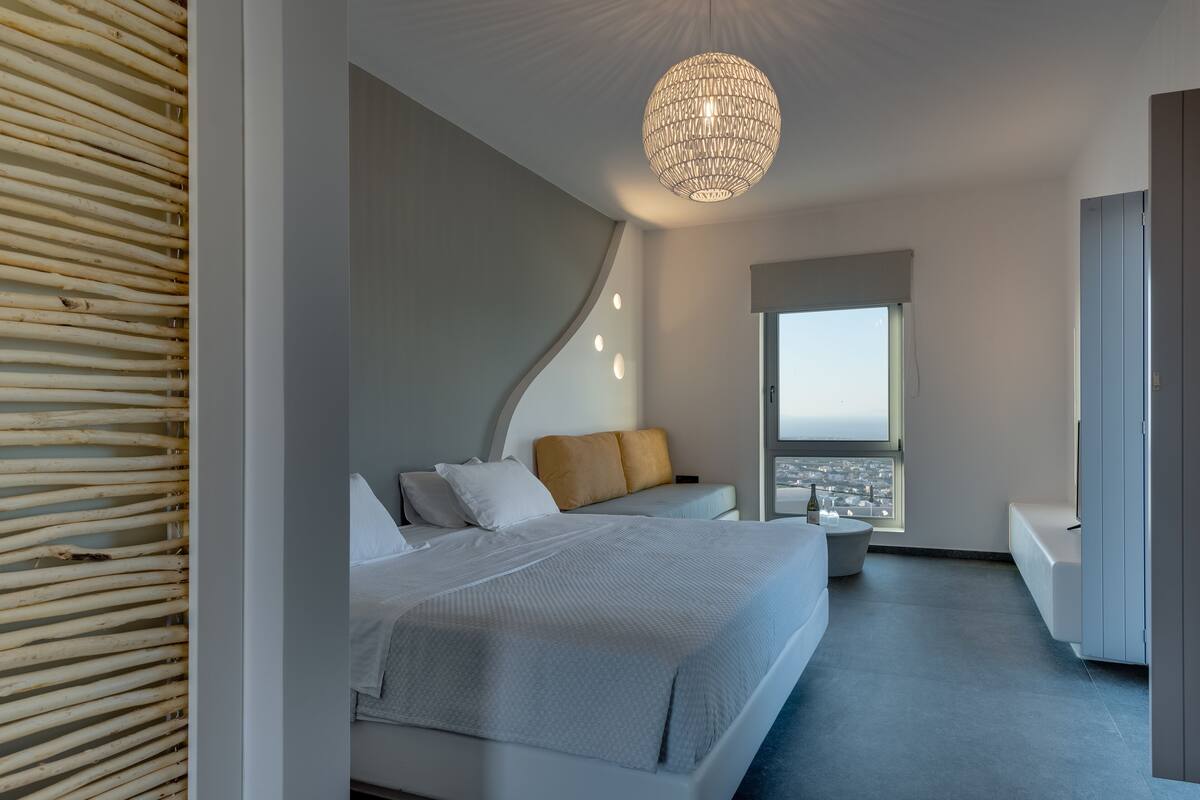 A modern bedroom with a large bed, a bedside table, a window with a view, and a unique ceiling light fixture.