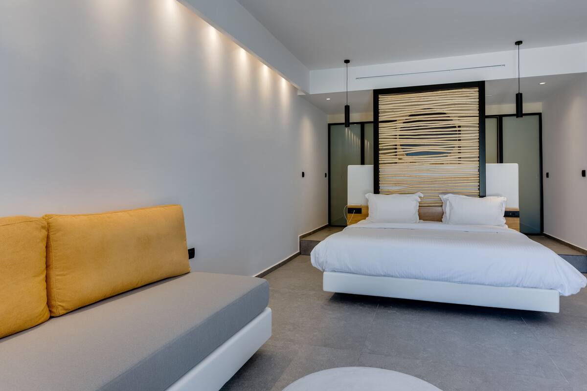 A modern hotel room with a large bed, a sofa, and a decorative wall panel.