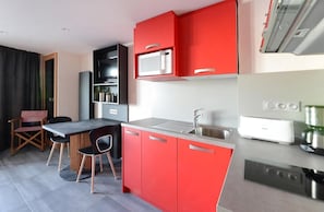 A modern kitchen with red cabinets, a black dining table, and a microwave.