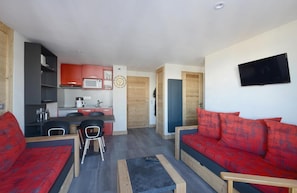 A compact living space with a kitchenette, a sofa set, and a flat-screen TV.