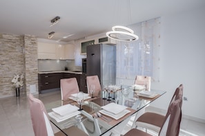 Un comedor moderno con una mesa de vidrio, sillas rosas y una cocina al fondo.