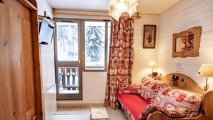 Ein gemütliches Zimmer mit einem hölzernen Bett, einem kleinen Tisch, einer Bank und einem Fenster mit Blick auf schneebedeckte Bäume.