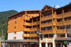 Un edificio de madera de varios pisos, con balcones, una tienda en la planta baja y montañas al fondo.