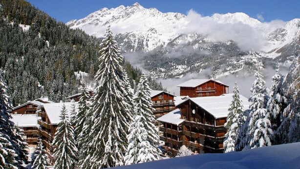 Ein schneebedecktes Bergresort mit Holzhäusern und Kiefern.