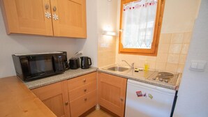 A compact kitchen with wooden cabinets, a microwave, a coffee maker, a sink, and a refrigerator.