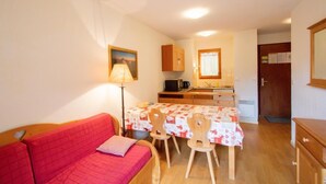 A compact living space with a red sofa, a dining table with chairs, a kitchen area with a microwave, and a small cabinet.