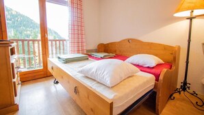 A wooden bed with white and red bedding, a bedside lamp, and a view of a balcony with a checkered curtain.