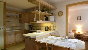 Cucina compatta con mobili in legno, forno a microonde, bollitore e zona pranzo con tavolo apparecchiato per due.