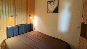 Makuuhuone, jossa on puinen sängynpääty, ruskea päiväpeite ja seinälle kiinnitetty taideteos.