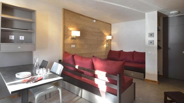 A modern hotel room with a wooden headboard, a dining table with cutlery, and a red sofa. - 100m from ski slopes, 8th floor, view ski slopes, balcony, tv, ski locker, 28m², La Plagne (La Plagne)