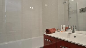 A modern bathroom with a white bathtub, a glass shower enclosure, and a vanity with a mirror. - 100m from ski slopes, 8th floor, view ski slopes, balcony, tv, ski locker, 28m², La Plagne (La Plagne)