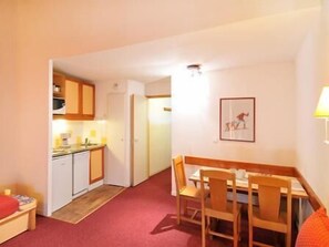 Une chambre d’hôtel compacte dotée d’une kitchenette, d’un coin repas avec des chaises en bois, d’une petite table et d’un tableau encadré au mur.