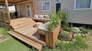 Een houten terras met een bank en een eettafel, omgeven door een tuin met verschillende planten en bloemen.