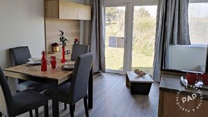 Een moderne eetruimte met een houten tafel en stoelen, een klein keukenhoekje met kastjes en een schuifdeur naar een buitenruimte.