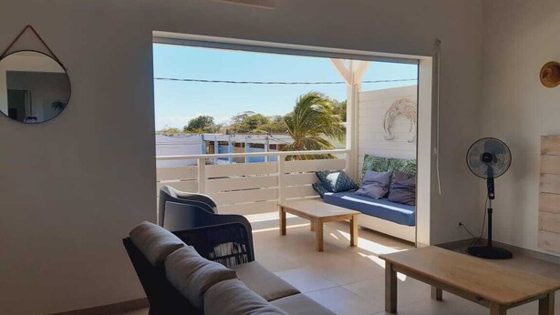 A modern living room with a sofa, a coffee table, and a fan. There is a large window with a view of the outside.