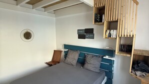 A bedroom with a bed, a wooden loft, and a shelf with books.