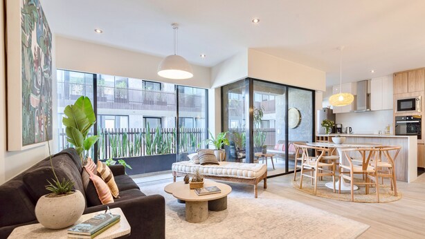 A modern living room with a sofa, coffee table, and dining area. There is a kitchen with wooden cabinets and a large window overlooking a balcony. - ✶ Maras Residence ✶ LUXURY Rooftop Pool & Grill (Miraflores)